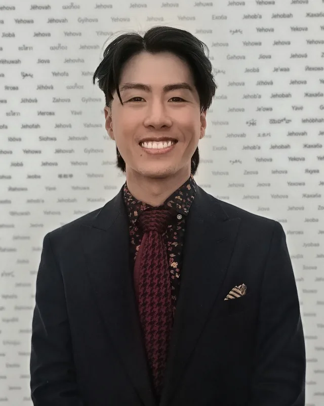 Huan Huynh, licensed massage therapist, smiling in a dark suit and tie